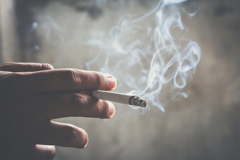 Hand holding lit cigarette with visible smoke